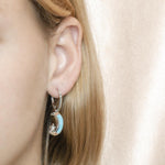The picture shows a model wearing a 925 sterling silver larimar moon and star lever-back earring.