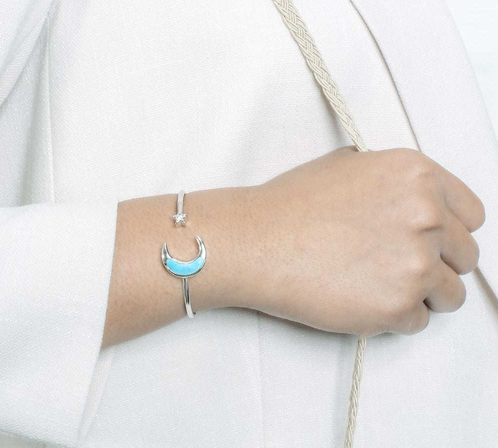 The picture shows a model wearing a 925 sterling silver larimar moon and star sleek bangle with topaz.