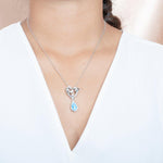 The picture shows a model wearing a sterling silver larimar dolphin pendant with a heart and wave motif, aquamarines, and topaz.
