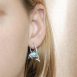 The picture shows a model wearing a 925 sterling silver larimar dolphin in a hoop earring with topaz