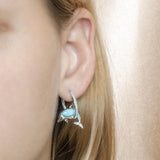 The picture shows a model wearing a 925 sterling silver larimar dolphin in a hoop earring with topaz