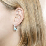 The picture shows a model wearing a 925 sterling silver larimar dolphin in a hoop earring with topaz