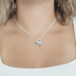 The picture shows a model wearing a 925 sterling silver larimar dolphin through circle pendant with topaz.