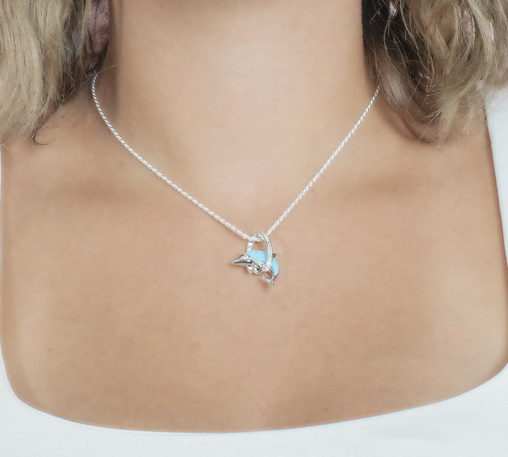 The picture shows a model wearing a 925 sterling silver larimar dolphin through circle pendant with topaz.