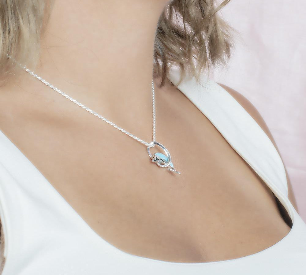 The picture shows a model wearing a 925 sterling silver larimar dolphin through circle pendant with topaz.