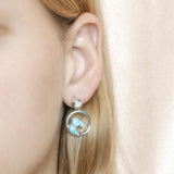 The picture shows a model wearing a 925 sterling silver larimar wave earring with topaz