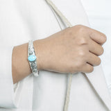 In this photo there is a model wearing a 925 sterling silver bangle with one blue larimar gemstone and plumeria engravings.