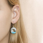 The picture shows a model wearing a large 925 sterling silver larimar ocean wave hook earring with topaz.