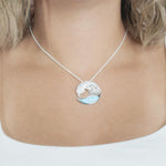 The picture shows a model wearing a 925 sterling silver larimar ocean wave pendant with topaz.
