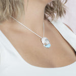 The picture shows a model wearing a 925 sterling silver larimar ocean wave pendant with topaz.