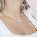 The picture shows a model wearing a 925 sterling silver larimar ocean wave pendant with topaz.