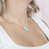 The picture shows a model wearing a 925 sterling silver larimar ocean wave pendant with topaz.