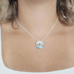 The picture shows a model wearing a 925 sterling silver larimar ocean wave pendant with topaz.