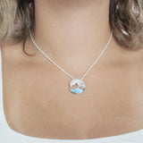 The picture shows a model wearing a 925 sterling silver larimar ocean wave pendant with topaz.