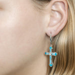 The picture shows a model wearing a 925 sterling silver larimar, opalite, and aquamarine cross earring.