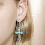 The picture shows a model wearing a 925 sterling silver larimar, opalite, and aquamarine cross earring.