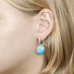 The picture shows a model wearing a 925 sterling silver larimar and opalite lever-back earrings