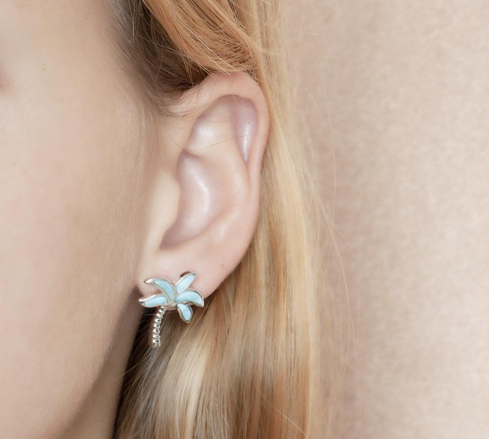In this photo there is a model wearing 925 sterling silver palm tree stud earrings with larimar gemstones.
