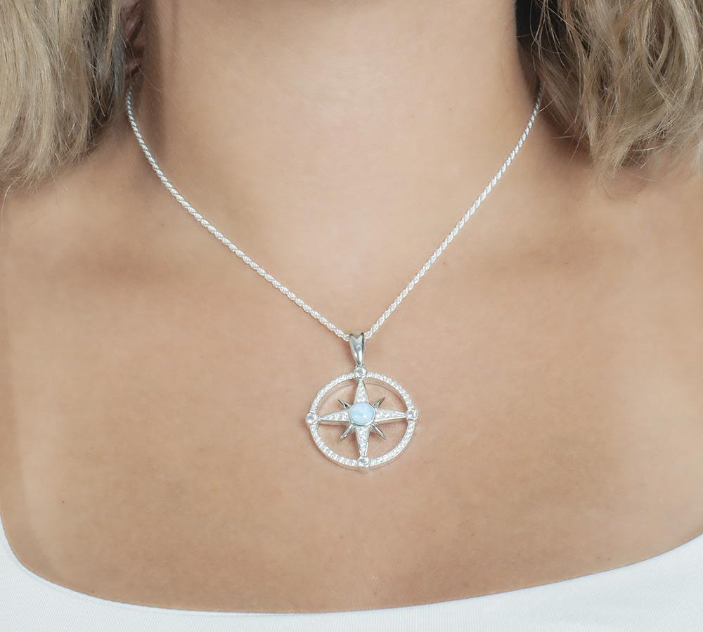In this photo there is model with blonde hair and a white shirt, wearing a sterling silver compass pendant with blue larimar and topaz gemstones.