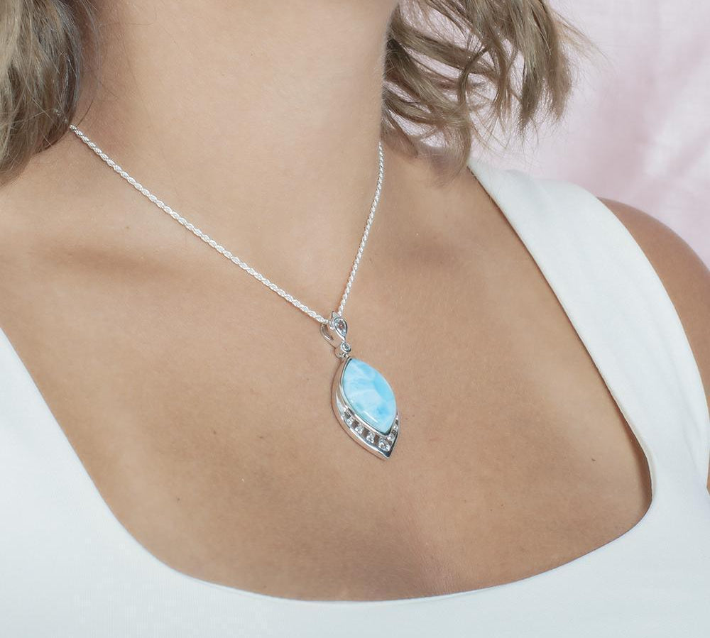 The picture shows a model wearing a 925 sterling silver larimar peacock feather pendant with topaz and aquamarine.