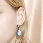 The picture shows a model wearing a 925 sterling silver larimar teardrop lever-back earrings with topaz.