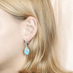 The picture shows a model wearing a 925 sterling silver larimar teardrop lever-back earrings with topaz.