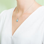 In this photo there is a model turned to the left with a white shirt, wearing a sterling silver pineapple pendant with one blue larimar gemstone.