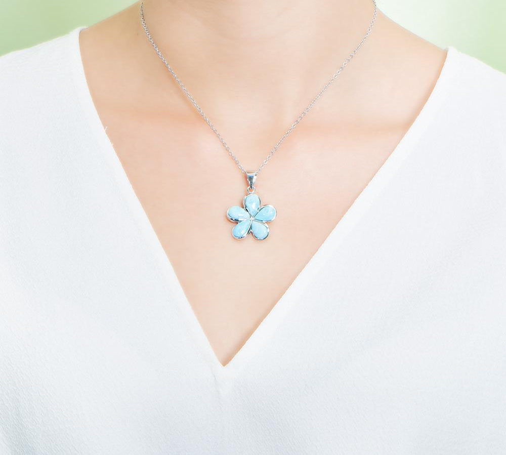 In this photo there is a model with a white shirt wearing a medium sized sterling silver plumeria pendant with blue larimar gemstones.