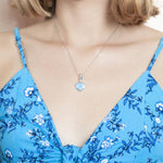 The picture shows a model wearing a 925 sterling silver larimar heart pendant and a blue dress.