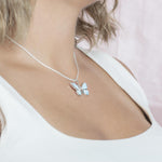 In this photo there is a model turned to the right with blonde hair and a white shirt, wearing a sterling silver butterfly pendant with blue larimar gemstones and aquamarine.