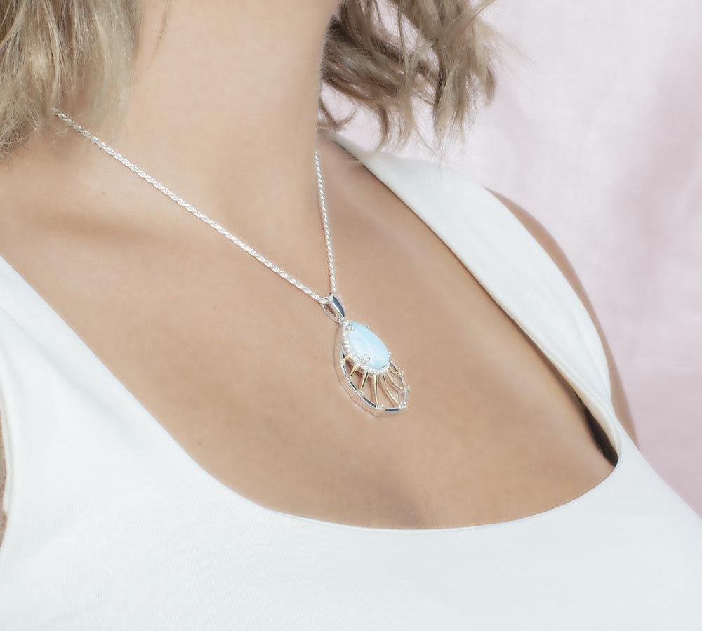 In this photo there is a model with blonde hair and a white shirt turned to the right, wearing a sterling silver and gold plated tear drop pendant with topaz, aquamarine, and one blue larimar gemstone.