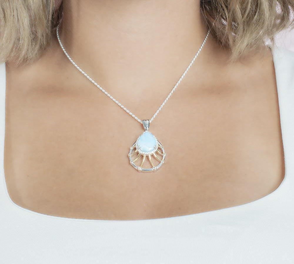 In this photo there is a model with blonde hair and a white shirt wearing a sterling silver and gold plated tear drop pendant with topaz, aquamarine, and one blue larimar gemstone.