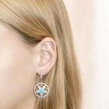 The picture shows a model wearing a 925 sterling silver larimar star lantern lever-back earring with topaz