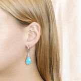The picture shows a model wearing a 925 sterling silver larimar starry sky teardrop lever-back earring with topaz.