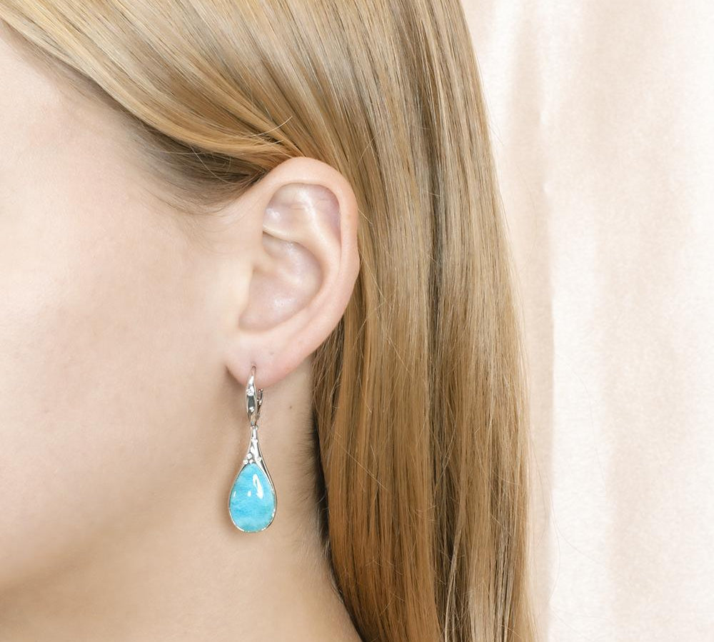 The picture shows a model wearing a 925 sterling silver larimar starry sky teardrop lever-back earring with topaz.