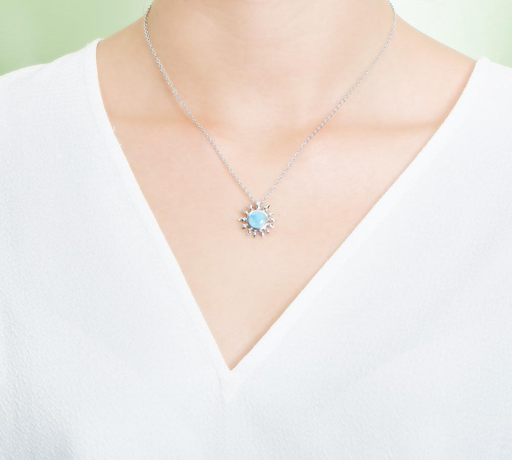 In this photo there is a model with a white shirt wearing a sterling silver sunflower pendant with one blue larimar gemstone.