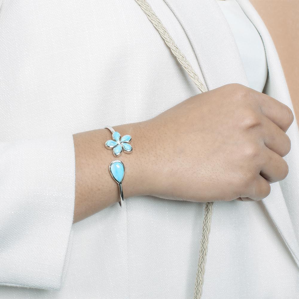 In this photo there is a model wearing a 925 sterling silver plumeria and teardrop pendant with blue larimar gemstones.