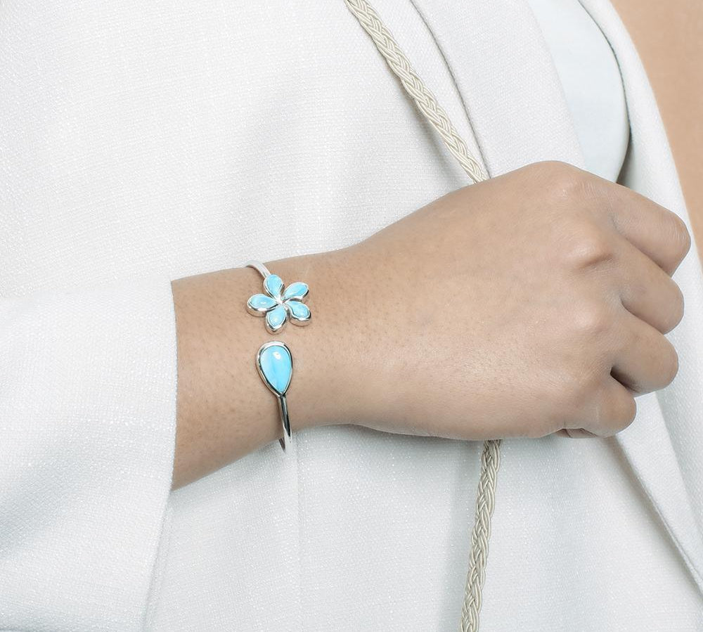 In this photo there is a model wearing a 925 sterling silver plumeria and teardrop pendant with blue larimar gemstones.
