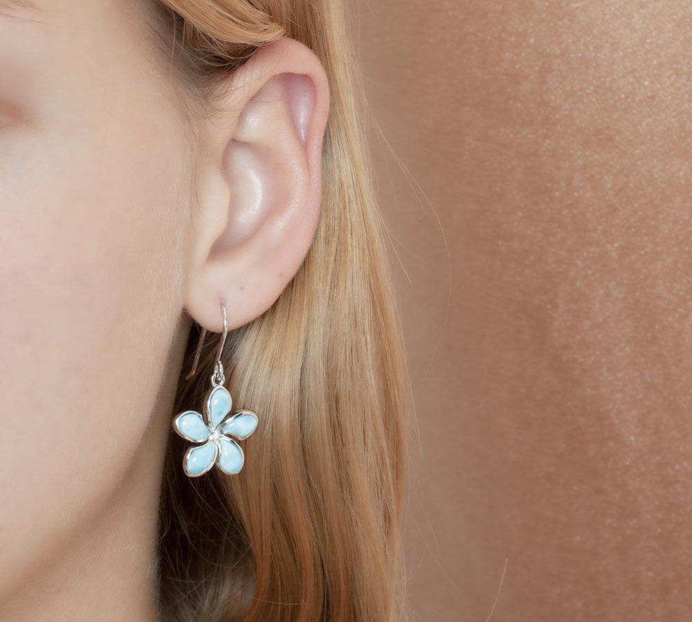 In this photo there is a model wearing a 925 sterling silver plumeria hook earring with blue larimar gemstones.