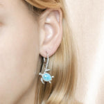 The picture shows a model wearing a 925 sterling silver larimar swimming sea turtle lever-back earring.