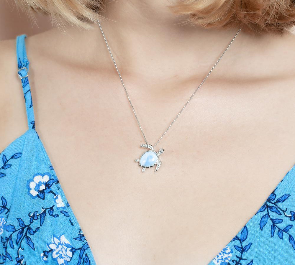 The picture shows a model wearing a 925 sterling silver larimar swimming sea turtle pendant.