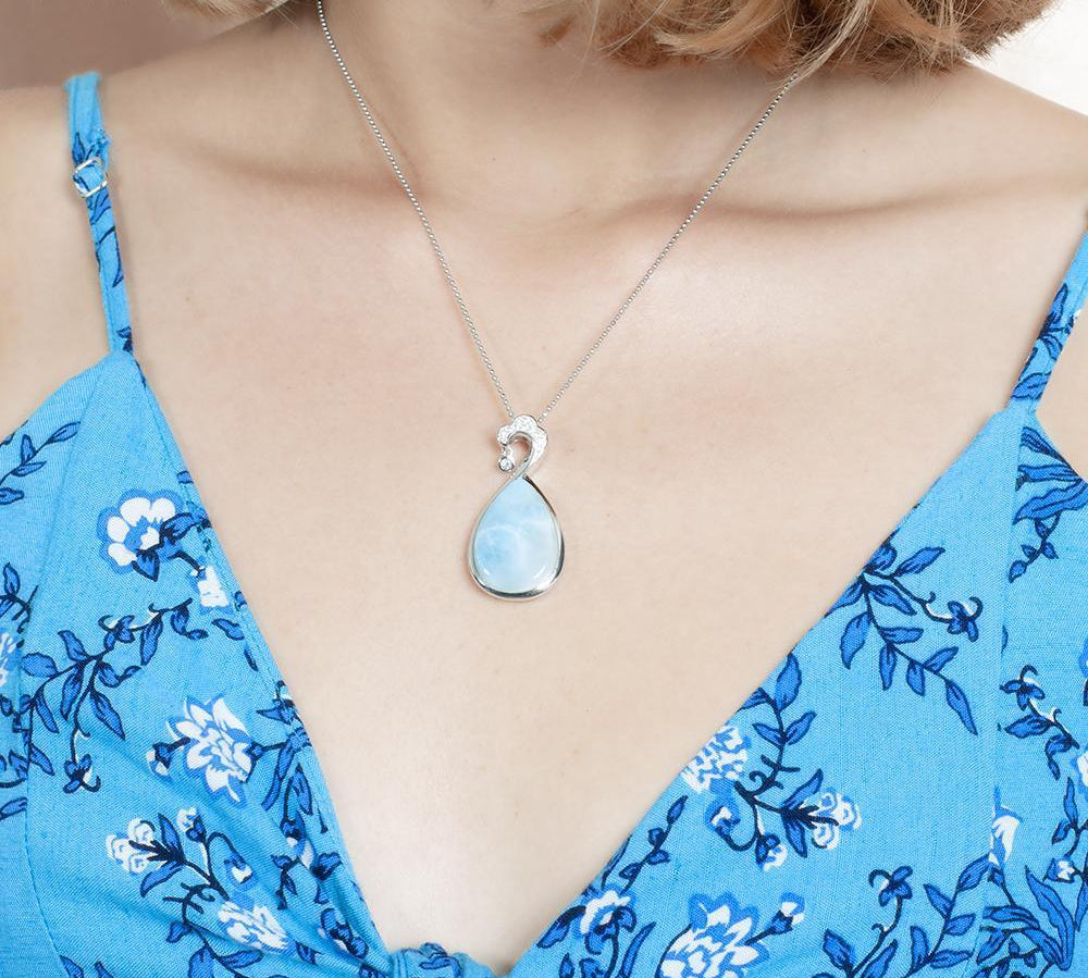The picture shows a model wearing a 925 sterling silver larimar teardrop wave pendant with aquamarine and topaz.