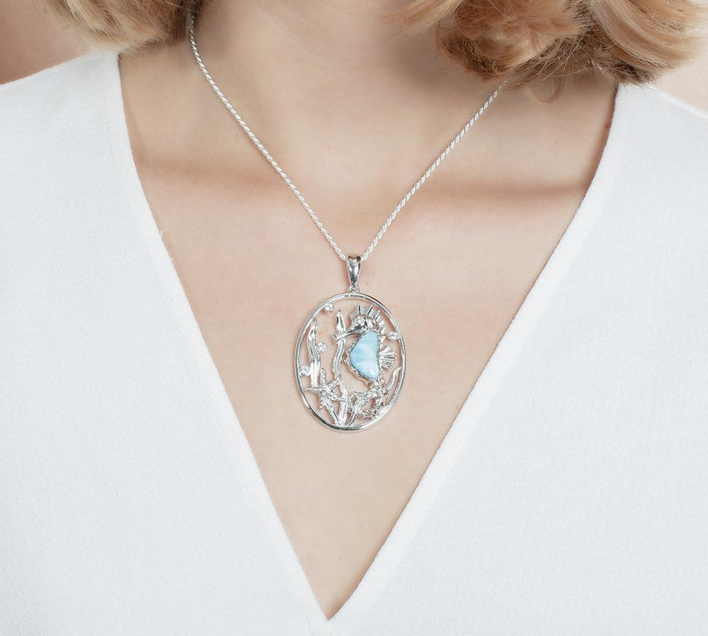 The picture shows a model wearing a 925 sterling silver pendant with a seahorse, starfish, and seaweed including a larimar gemstone and cubic zirconia.