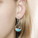 The picture shows a model wearing a 925 sterling silver larimar whale wave lever-back earring with topaz.
