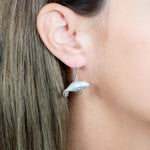 The picture shows a model wearing a 925 sterling silver manatee hook earring with topaz