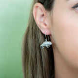 The picture shows a model wearing a 925 sterling silver manatee hook earring with topaz