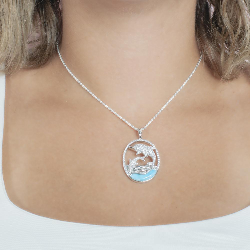 The picture shows a model wearing a 925 sterling silver two swimming dolphins pendant with a larimar gemstone and cubic zirconia.