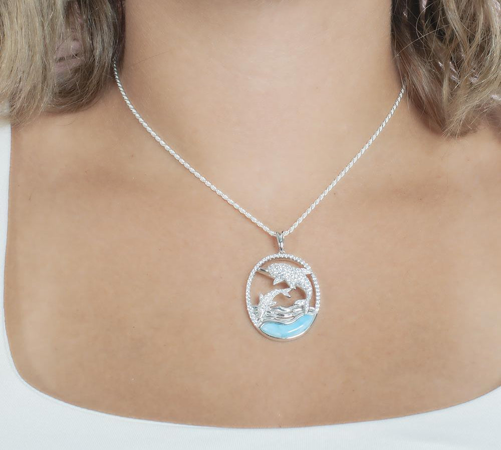 The picture shows a model wearing a 925 sterling silver two swimming dolphins pendant with a larimar gemstone and cubic zirconia.