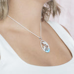 The picture shows a model wearing a 925 sterling silver two swimming dolphins pendant with a larimar gemstone and cubic zirconia.