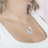 The picture shows a model wearing a 925 sterling silver two swimming dolphins pendant with a larimar gemstone and cubic zirconia.